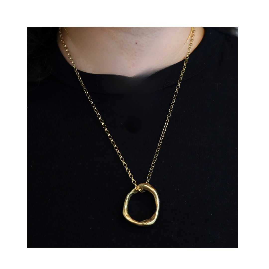 A person wears the Bough Necklace by Madeleine Sculptural Jewellery—a gold-plated brass chain with a large, irregular pendant—showcasing handmade jewelry against a black shirt background.