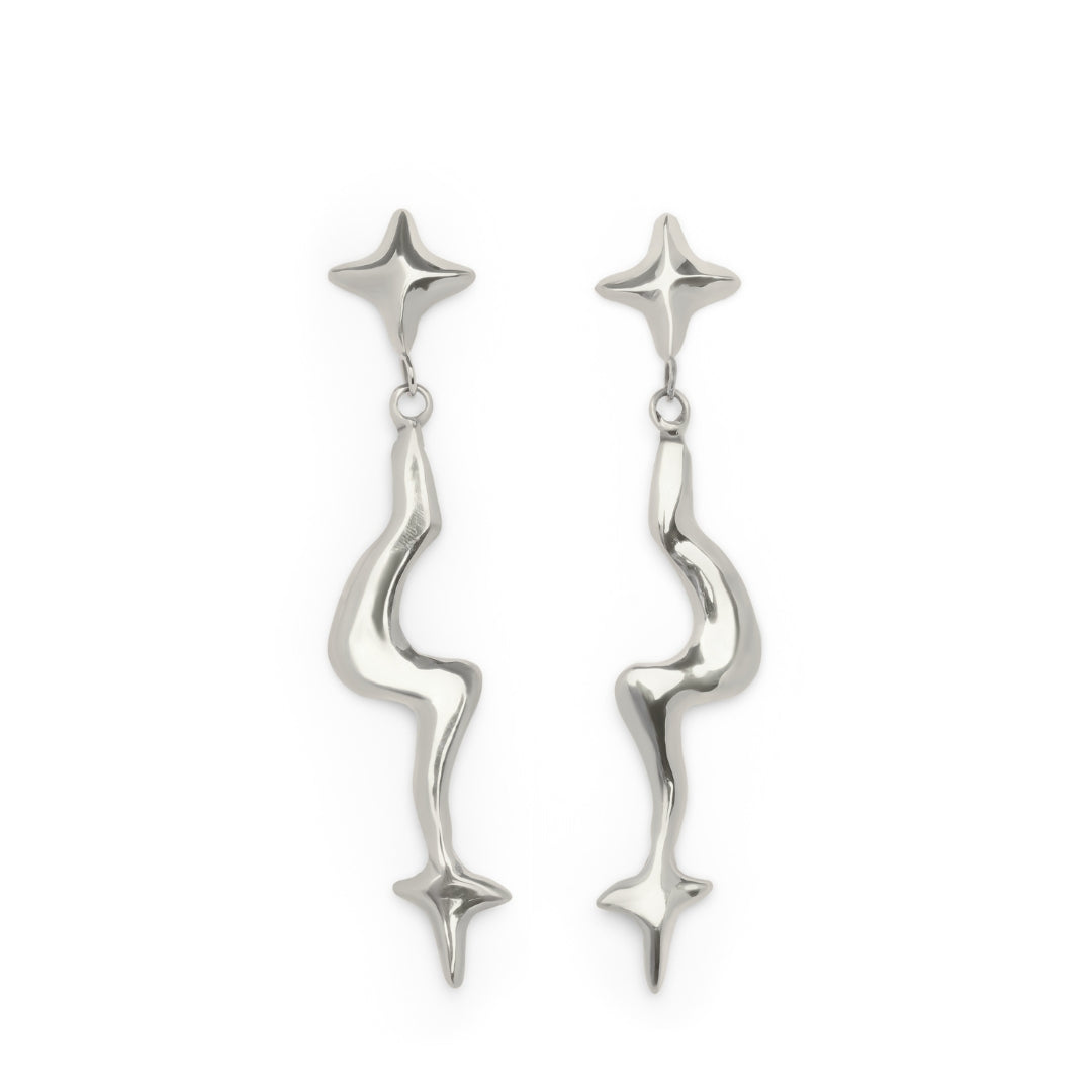A pair of Madeleine Blaine’s Nova Earring Large in shiny silver, featuring abstract wavy shapes accented with star-like designs at both the top and bottom.