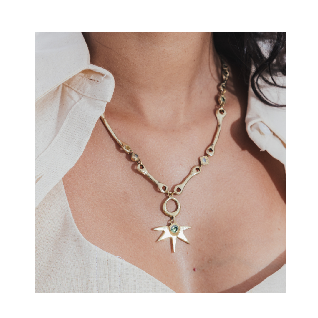 A close-up of a person wearing a cream-colored shirt and the Madeleine Sculptural Jewellery Réalta Necklace with Moissanite—a gold necklace featuring a star-shaped pendant with gemstone accents.