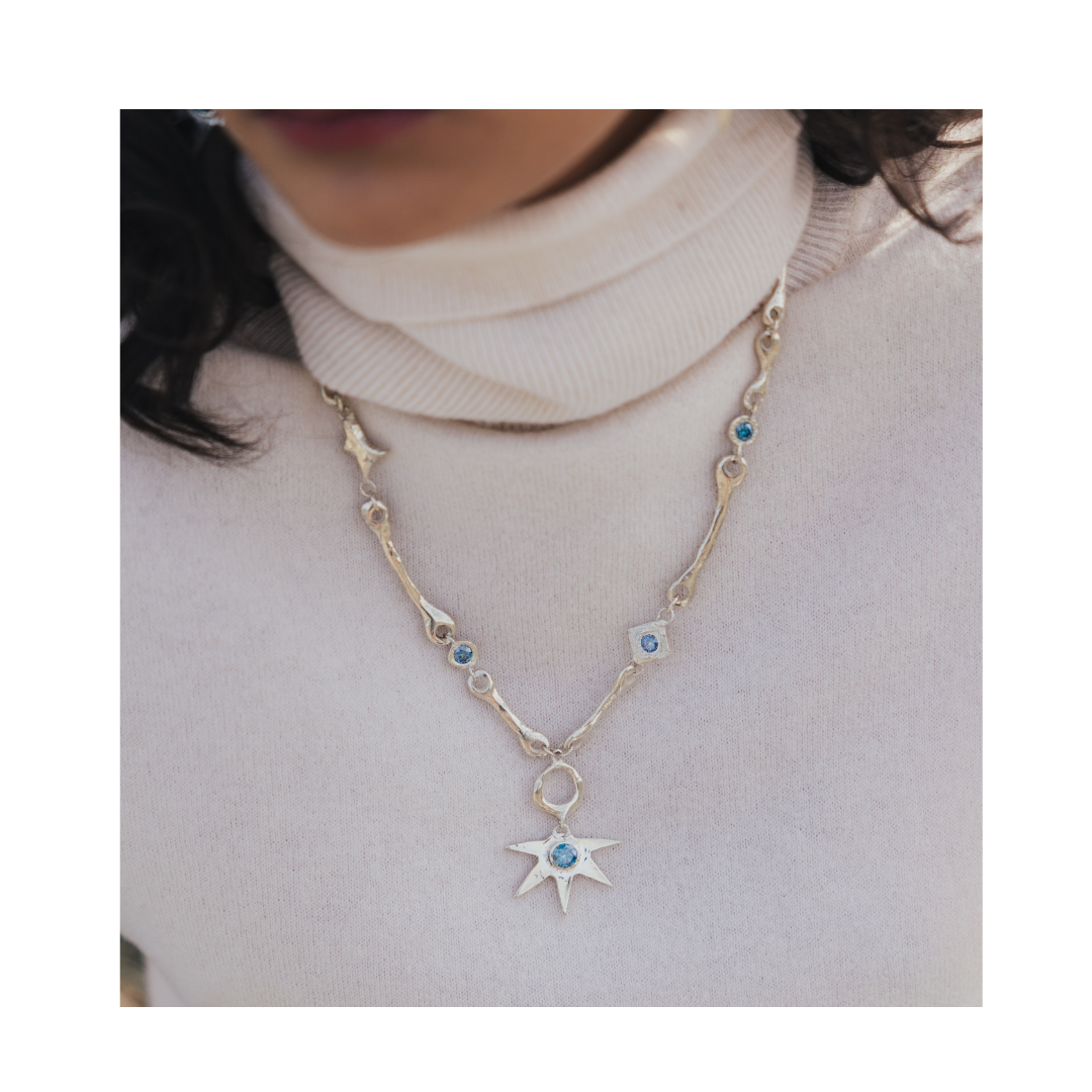 A person wearing a cream turtleneck sweater and the Réalta Necklace with Moissanite by Madeleine Sculptural Jewellery.