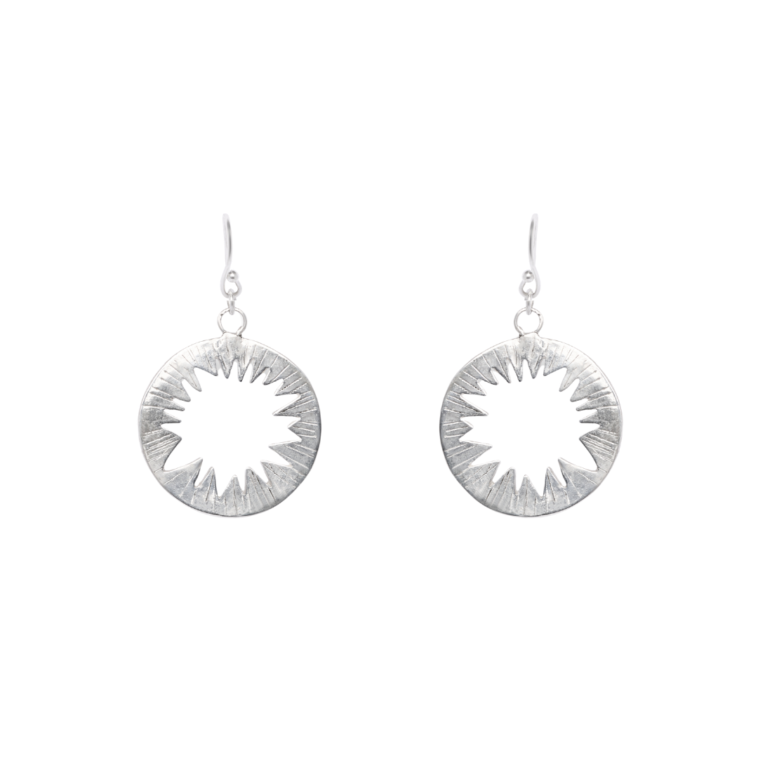 Introducing the Tundra Earrings by Madeleine Sculptural Jewellery—circular silver earrings with a striking cut-out starburst design, elegantly showcased on a plain white background.