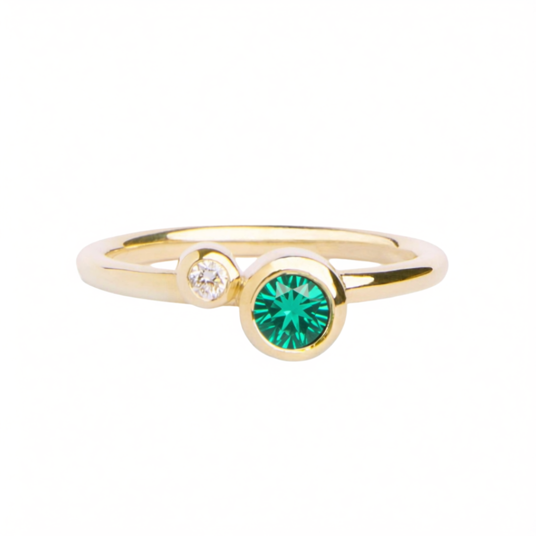 The Willow Shimmer 9ct yellow gold ring with Green Tsavorite & Diamond by Madeleine Fine Jewellery features a small round white diamond set beside a larger round green tsavorite gemstone on a delicate yellow gold band, beautifully showcased against a whit
