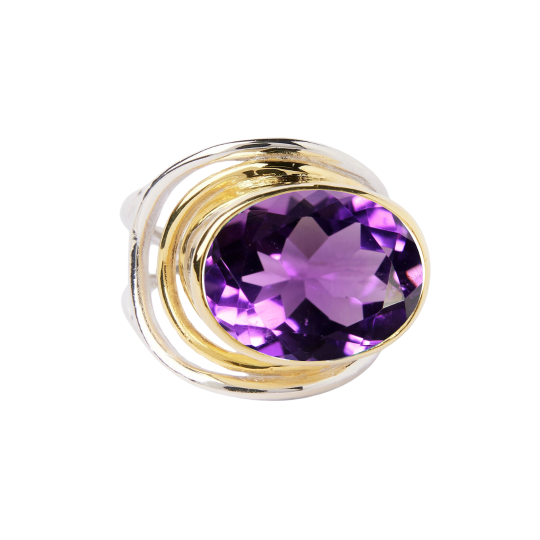 The Party Ring by Gallardo & Blaine Designs features a gold adjustable band with a large oval purple gemstone set in a swirl design, sparkling brilliantly against the white background and offering a stunning statement accessory.