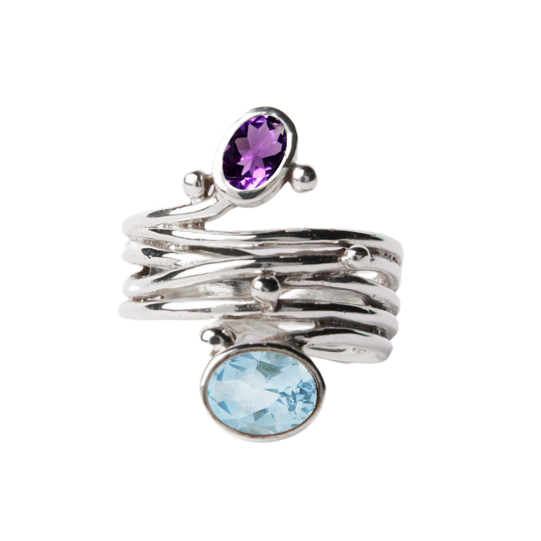The Snake Ring in Silver from Gallardo & Blaine Designs has a wavy, stacked design and features two oval gemstones: purple amethyst on top and light blue aquamarine at the bottom.