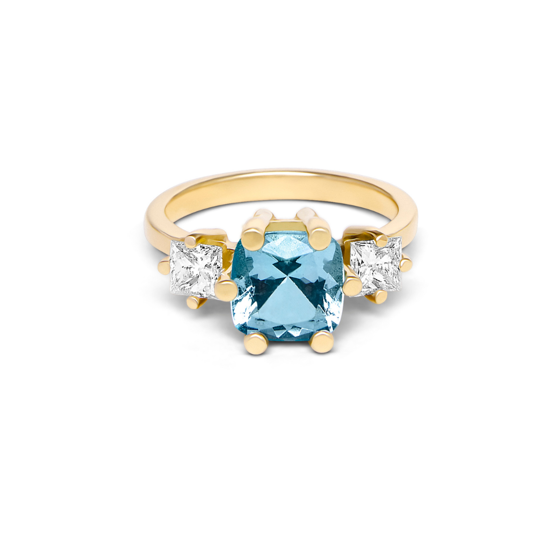 The Sky's Devotion 18ct Yellow Gold Ring by Madeleine Fine Jewellery features a striking square blue gem flanked by two clear stones—an elegant aquamarine engagement ring ideal for any occasion.