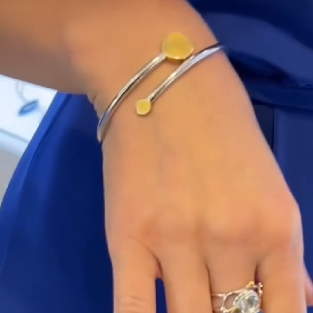 A hand wears the Archeol Bangle by Gallardo & Blaine Designs in sterling silver with gold accents, paired with a silver ring set with a clear gemstone, styled against a royal blue outfit for elegant Irish-inspired flair.