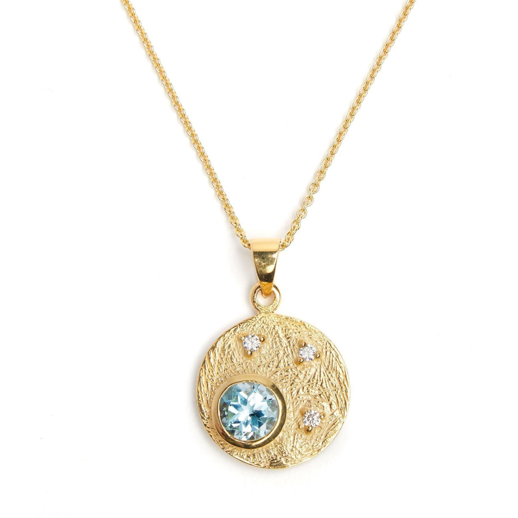 Gold Celeste Necklace in Gold & various gemstones featuring a circular pendant with a textured surface, a large blue gemstone in the center, and three smaller cubic zirconia gemstones arranged around it. The gemstone pendant is attached to a delicate gold