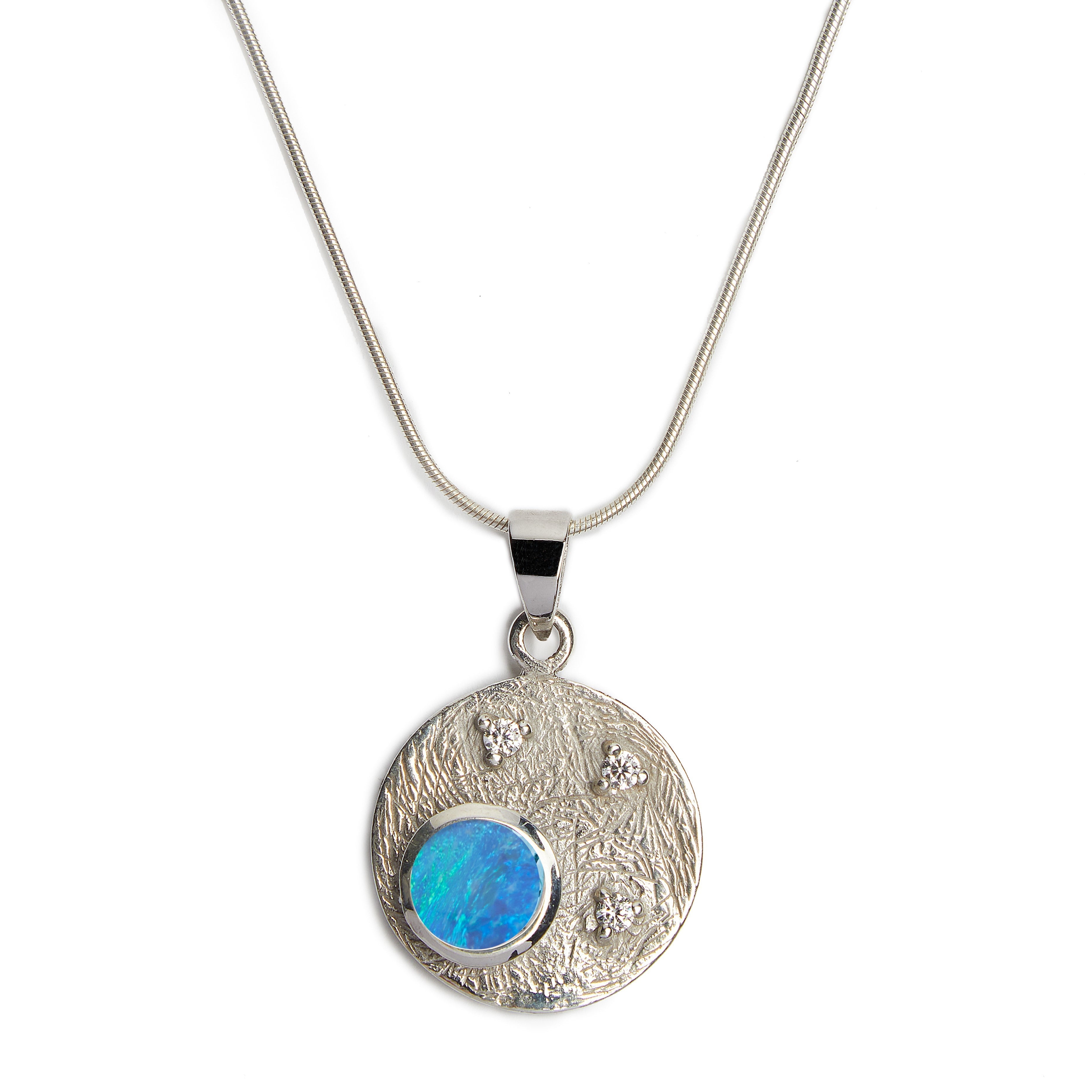 The Celeste Necklace in Silver & various gemstones by Gallardo & Blaine Designs is a stunning piece featuring a round pendant with an iridescent blue-green stone set in the lower left, surrounded by three small cubic zirconia accents. The chain is simple 