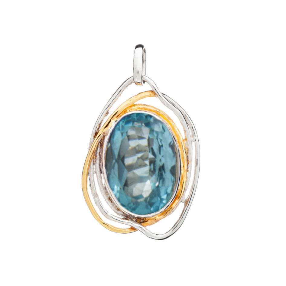 The statement gemstone pendant, known as the Cosmos Pendant Large in various gemstones by Gallardo & Blaine Designs, features an oval blue gemstone with a faceted surface set in a mixed metal frame. The frame boasts intertwining silver and gold-toned loop