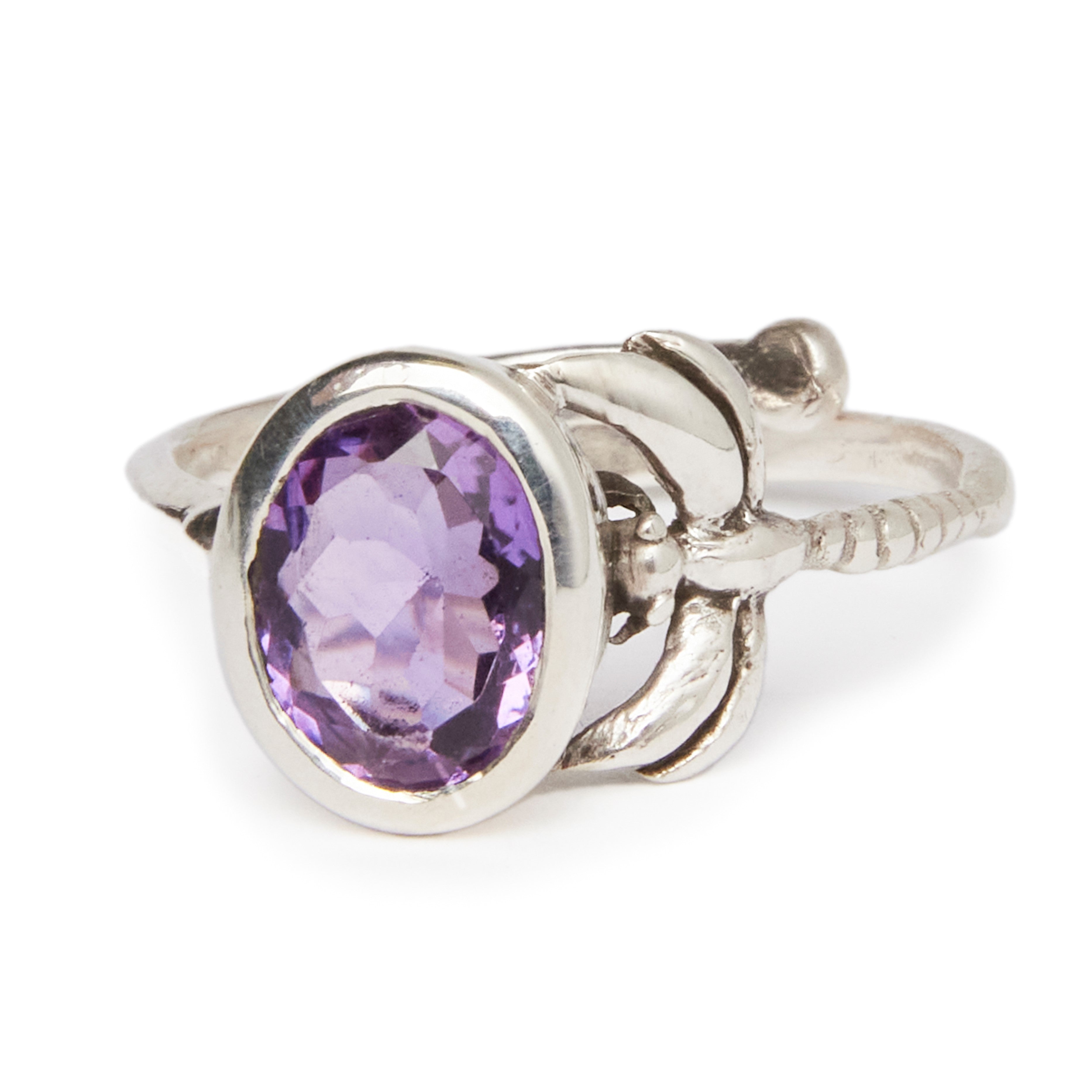 A timeless piece, the Daydream Ring in various gemstones by Gallardo & Blaine Designs features a large oval-shaped purple gemstone as its centerpiece. The band boasts ornate detailing resembling leaves around the gemstone setting, and its faceted cut ensu