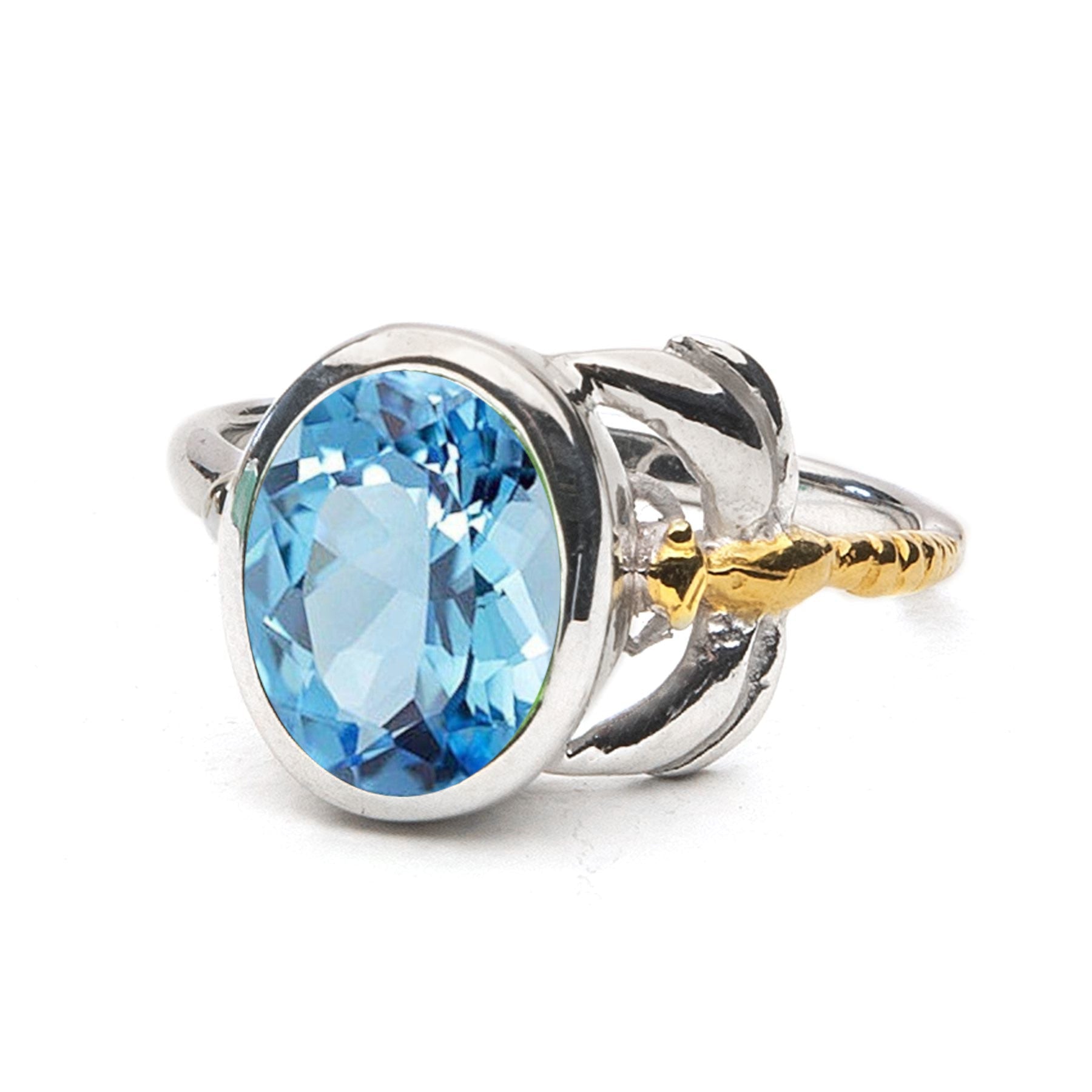 A timeless piece, the Daydream Ring in various gemstones by Gallardo & Blaine Designs features a large, oval-shaped blue gemstone in the center. The gemstone is encased in a polished silver setting and flanked by delicate metalwork resembling leaves or pe