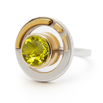 The Elodie Ring in Silver Gold & various gemstones from Gallardo & Blaine Designs is a silver masterpiece featuring a round, vibrant green gemstone set in the center. Surrounded by circular metallic designs in silver and gold tones, it combines vintage st