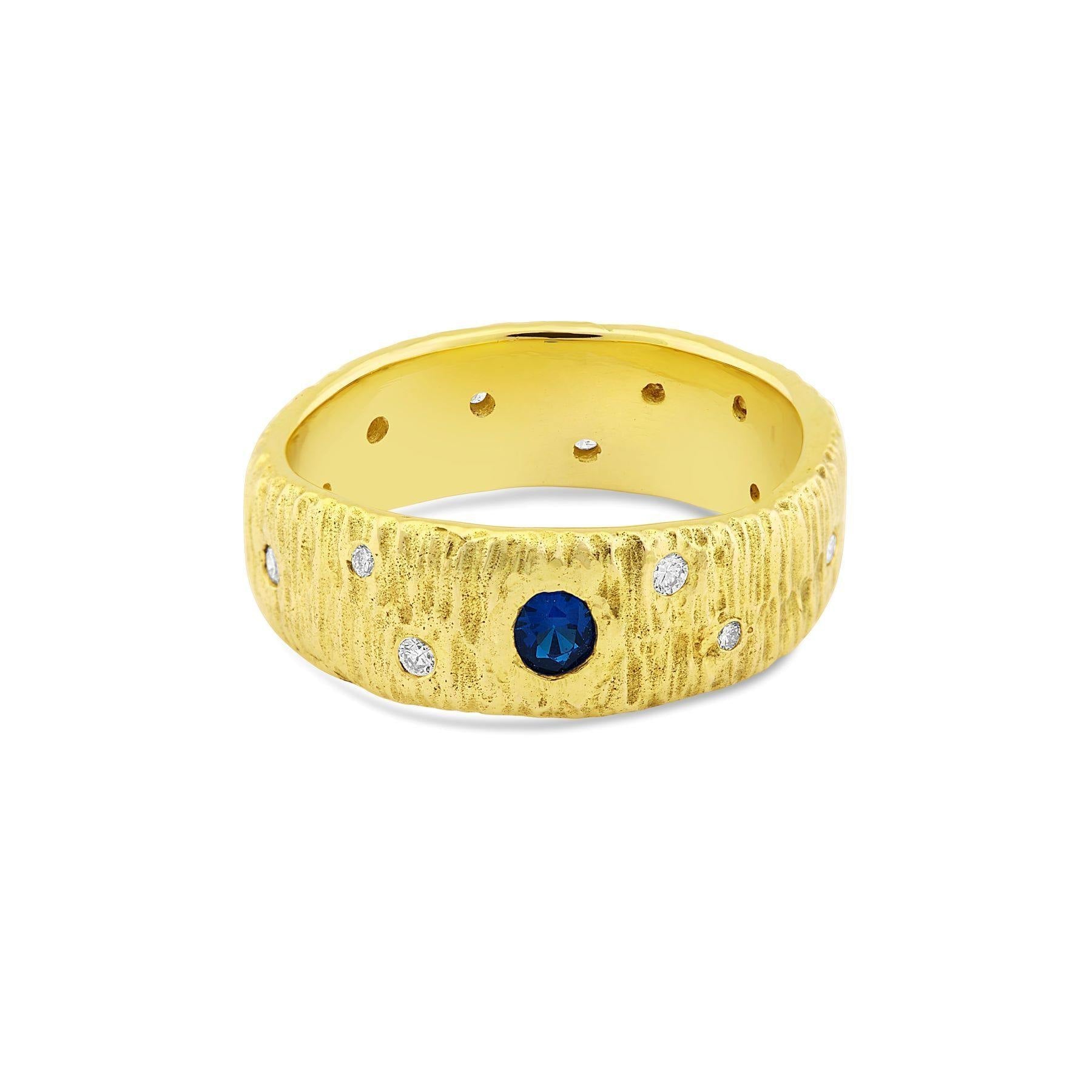 A textured 9 ct yellow gold ring featuring a central real sapphire is surrounded by six small white diamonds, evenly spaced around the ring's circumference. The inner band is smooth with small, evenly spaced holes. The Etta Ring with Sapphire & Diamonds f