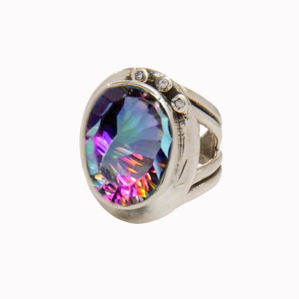 The Eyetelia Ring in various gemstones by Gallardo & Blaine Designs features a large, multicolored iridescent oval gemstone at its center. The wide band, designed with an adjustable design, splits into three parts near the top and is adorned with three sm