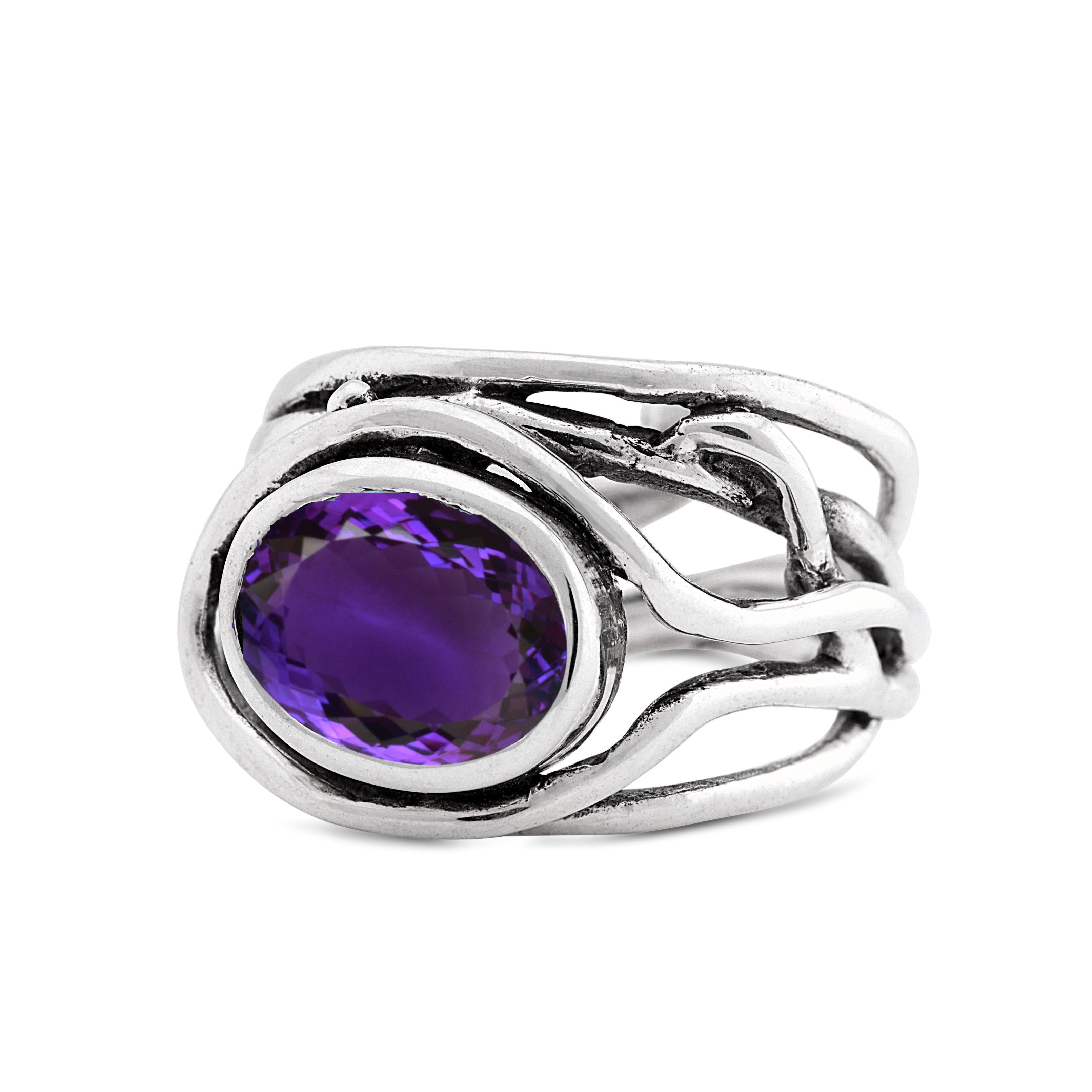 A Fossil Ring in silver & various gemstones by Gallardo & Blaine Designs with an intricate design featuring a large oval purple gemstone in the center. The band is composed of several intertwining silver strands, creating a unique and elegant look. This e