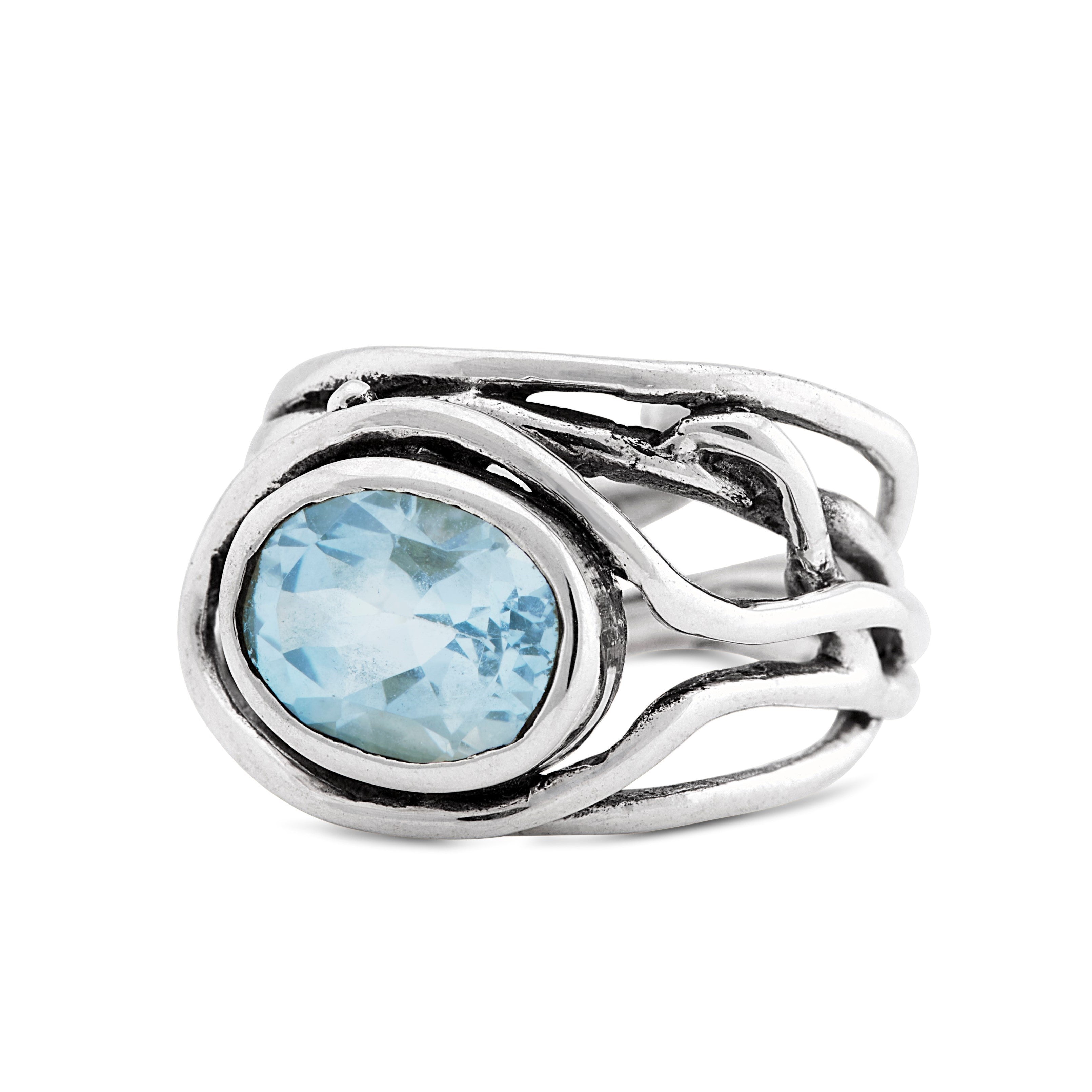 A Fossil Ring in silver & various gemstones by Gallardo & Blaine Designs with an intricate, intertwined band design featuring a large, oval-shaped, light blue gemstone at its center. The band twists around the gemstone in a unique, artistic fashion, makin