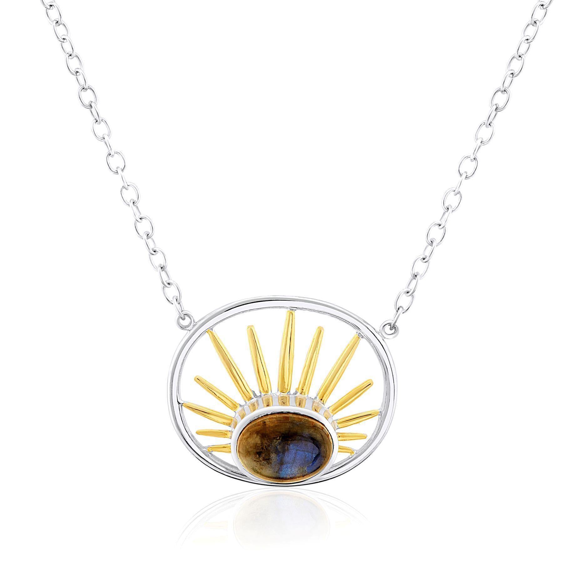A sterling silver necklace with a circular pendant displays golden sun rays emanating from a central dark gemstone. The pendant features an open circular frame, and the chain is adorned with small round links. This exquisite piece by Gallardo & Blaine Des