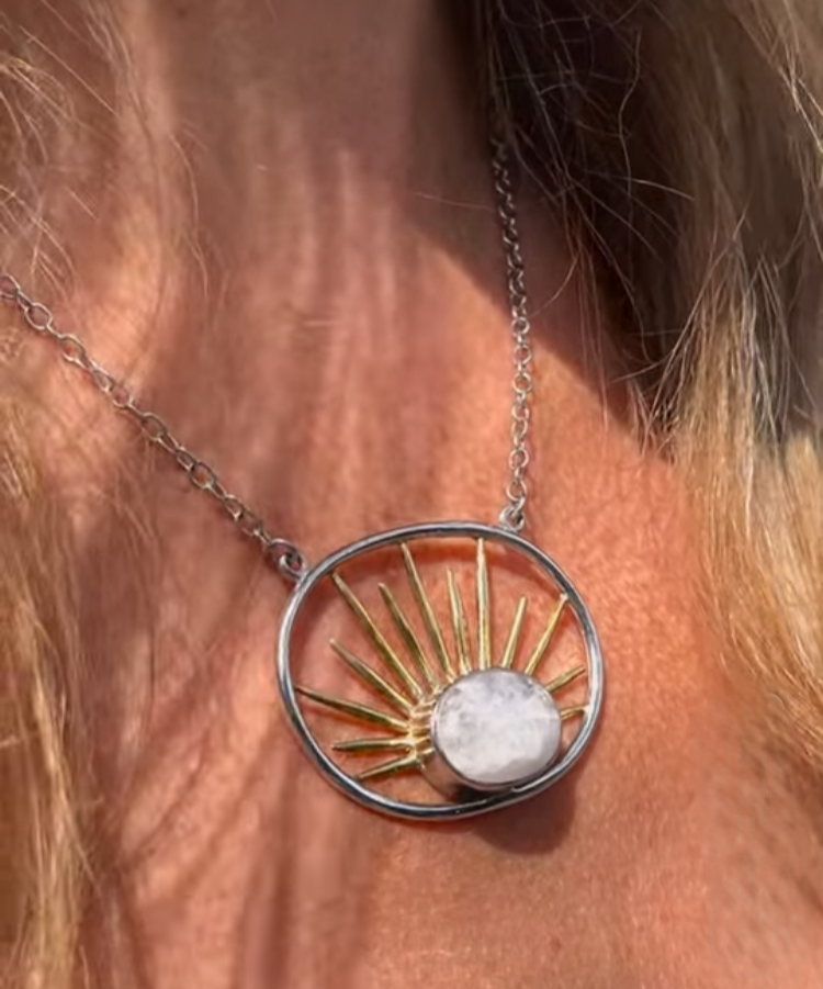 The Gallardo & Blaine Designs Goddess Necklace Large in Various Gemstones features a gold vermeil chain with a circular pendant adorned with gold sun rays and a white stone, shown worn elegantly around the neck.