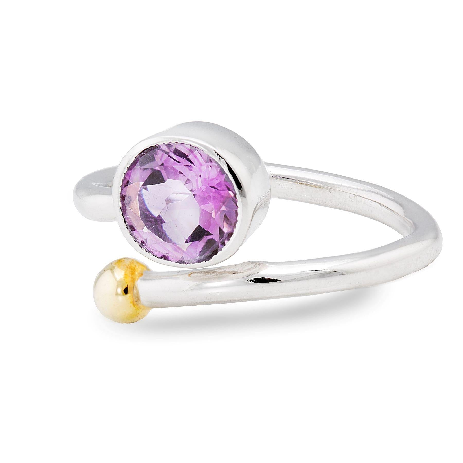 A close-up image of an elegant Honeysuckle Ring in Silver Gold & gemstones by Gallardo & Blaine Designs featuring a purple gemstone as its central focal point. The silver and gold jewelry piece has an open-ended band adorned with a small gold sphere at on