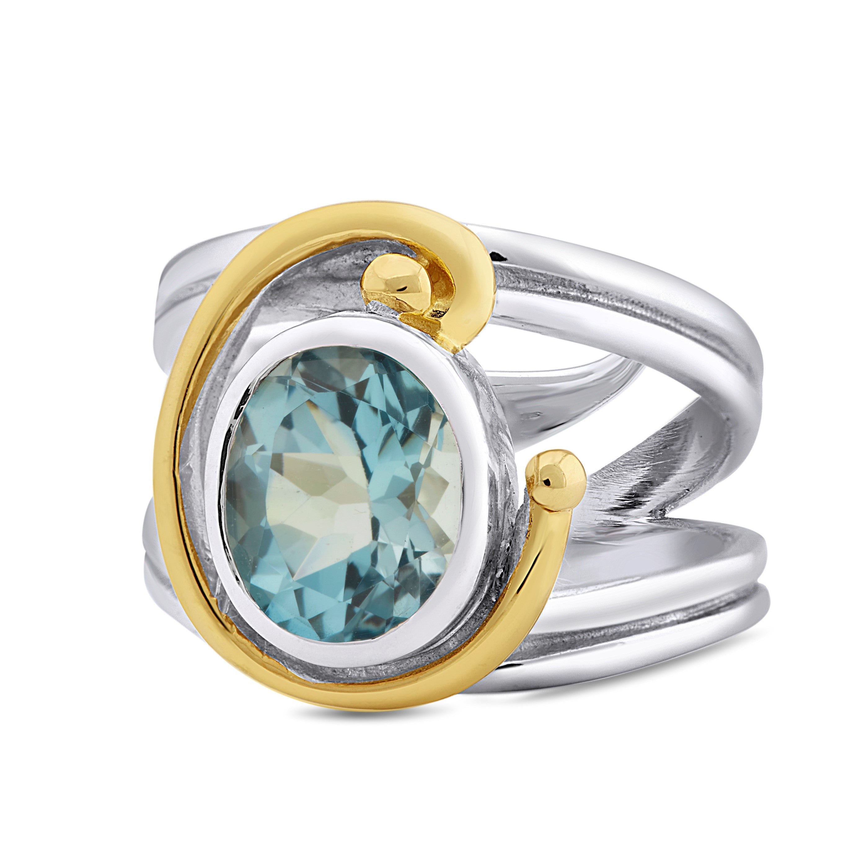 A silver ring with a split shank design features an oval blue gemstone encircled by a gold-tone spiral accent. This Jasmine Ring in various gemstones from Gallardo & Blaine Designs combines both silver and gold tones, giving it a unique and elegant appear