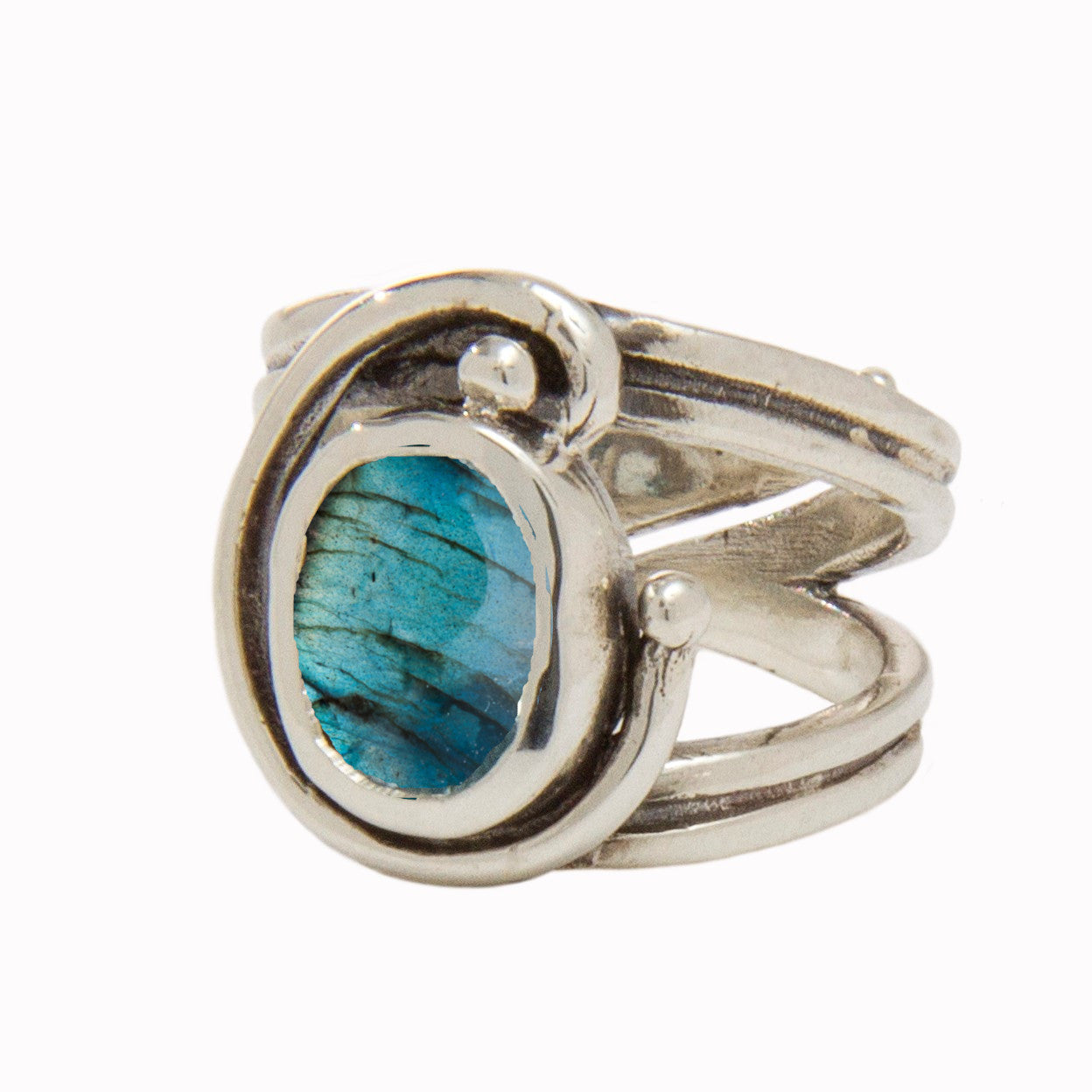 The Jasmine Ring in various gemstones by Gallardo & Blaine Designs features an intricate design with a prominent blue-green oval gemstone at the center. The band splits into decorative swirls encircling the gemstone, showcasing a unique and artistic style