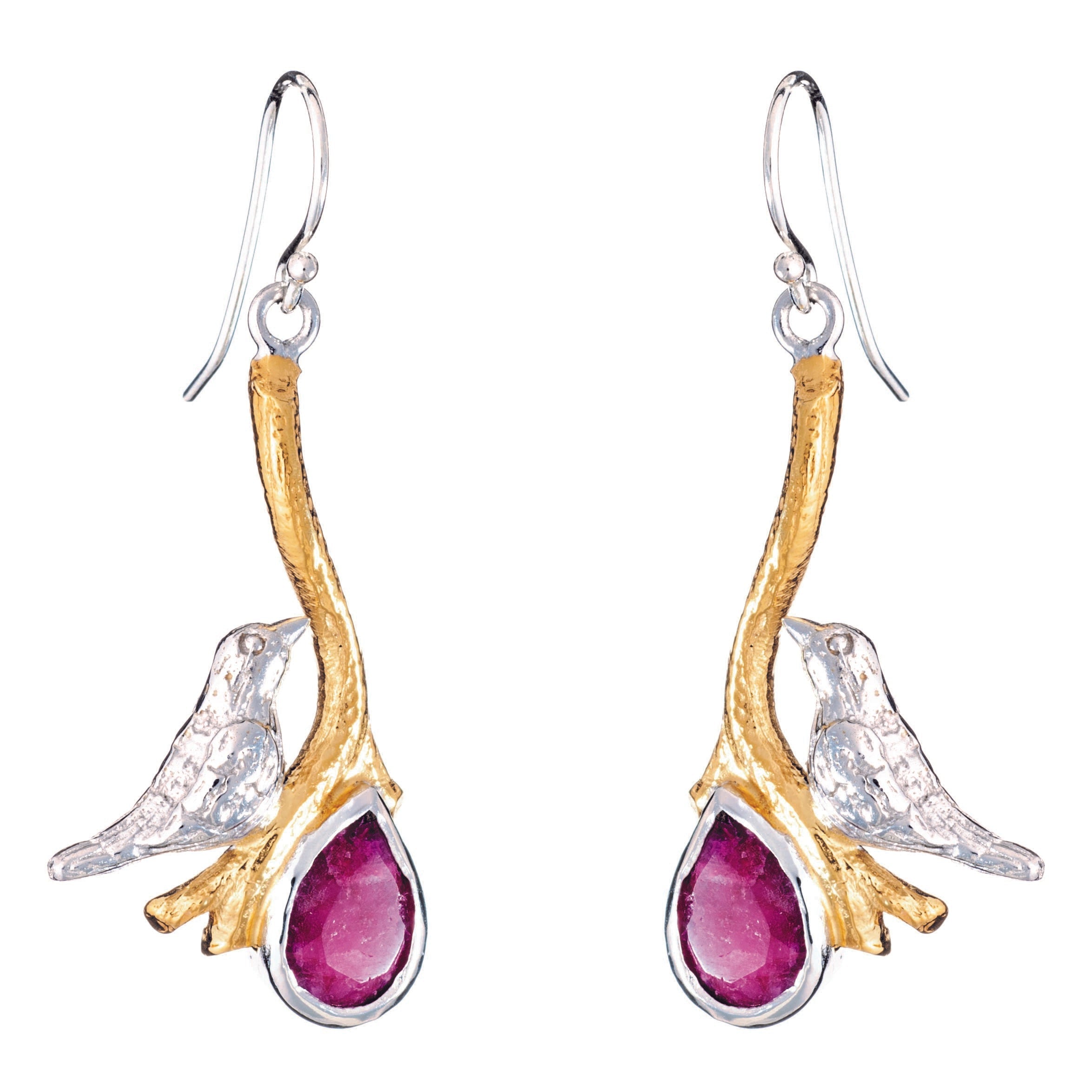 A pair of Lovebird Earrings in various gemstones from Gallardo & Blaine Designs features golden branches with silver birds perched on them, holding drop-shaped, deep red gemstones. The birds and branches are detailed with a shiny silver finish, while the 