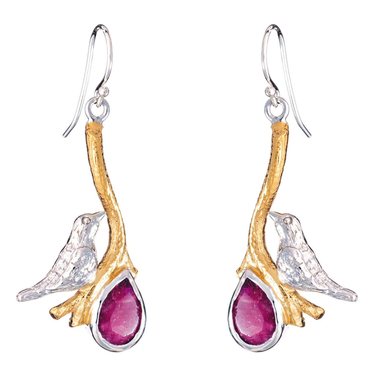 A pair of Lovebird Earrings in various gemstones from Gallardo & Blaine Designs features golden branches with silver birds perched on them, holding drop-shaped, deep red gemstones. The birds and branches are detailed with a shiny silver finish, while the 