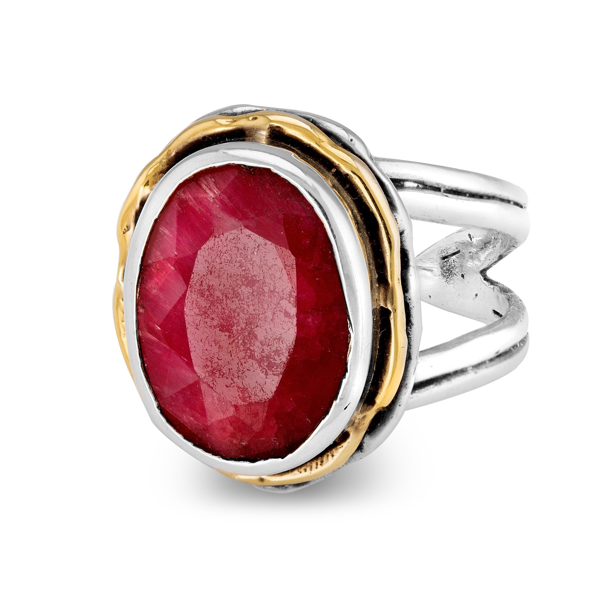 The Magnolia Ring in silver gold & various gemstones by Gallardo & Blaine Designs is a sterling silver piece featuring a large, faceted oval red gemstone prominently set in the center. Encircled by a gold-toned bezel on a split silver band, this statement