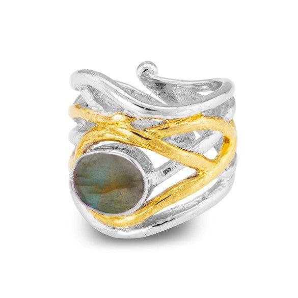 A chunky statement ring with an intricate design featuring intertwined silver and gold bands, crowned with a round, iridescent labradorite gemstone. The Mayhem Ring in various gemstones by Gallardo & Blaine Designs displays a range of colors when viewed f