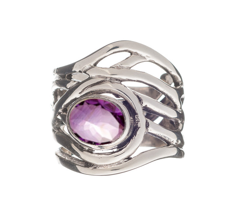 A Gallardo & Blaine Designs Mayhem Ring in various gemstones, featuring an intricate, wavy band design with a large oval-shaped purple gemstone set in the center. The chunky statement ring has a faceted gemstone that adds a reflective quality to the piece