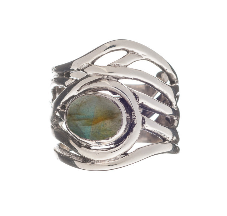 The Mayhem Ring in various gemstones by Gallardo & Blaine Designs features an intricate, wavy band design holding a central round labradorite gemstone with a blue-green iridescent hue. This adjustable ring has a modern, artistic appearance that brings a t