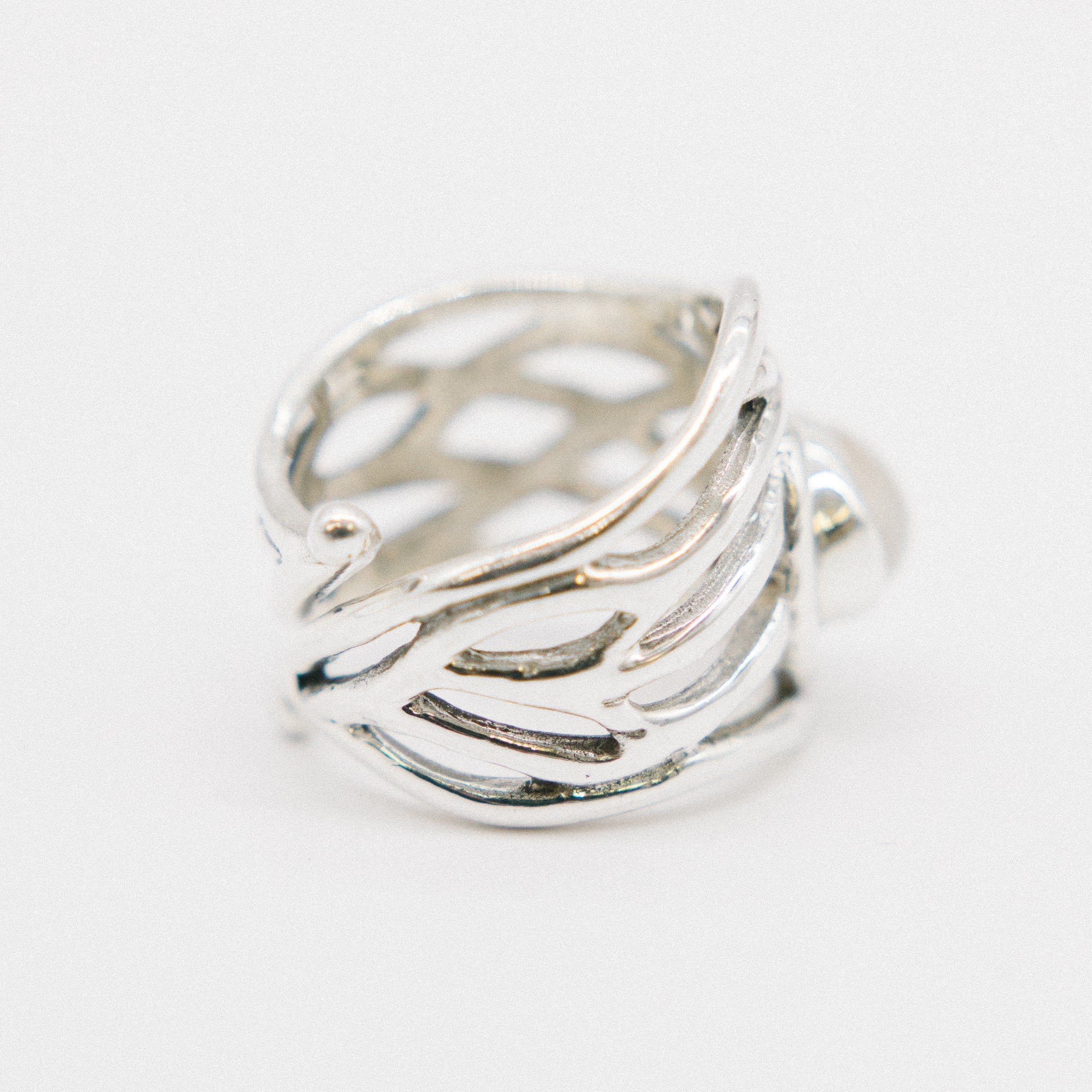 A close-up image of a chunky statement ring with an intricate, openwork design. The band features a pattern resembling interwoven strands, giving it a light and airy appearance. The Mayhem Ring in various gemstones by Gallardo & Blaine Designs is position