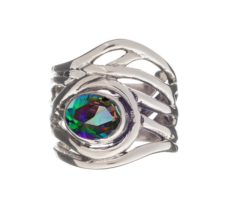 A close-up of the Mayhem Ring in various gemstones by Gallardo & Blaine Designs, featuring an intricate, wavy band design and a central, multifaceted gemstone that displays a gradient of green, purple, and blue colors. The detailed craftsmanship of the me