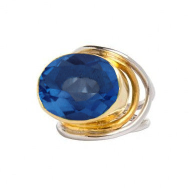 A Party Ring in various gemstones by Gallardo & Blaine Designs featuring a large, oval-shaped blue gemstone. The statement gemstone is set in a gold bezel with sterling silver bands artistically wrapping around it, creating an elegant and vibrant accessor