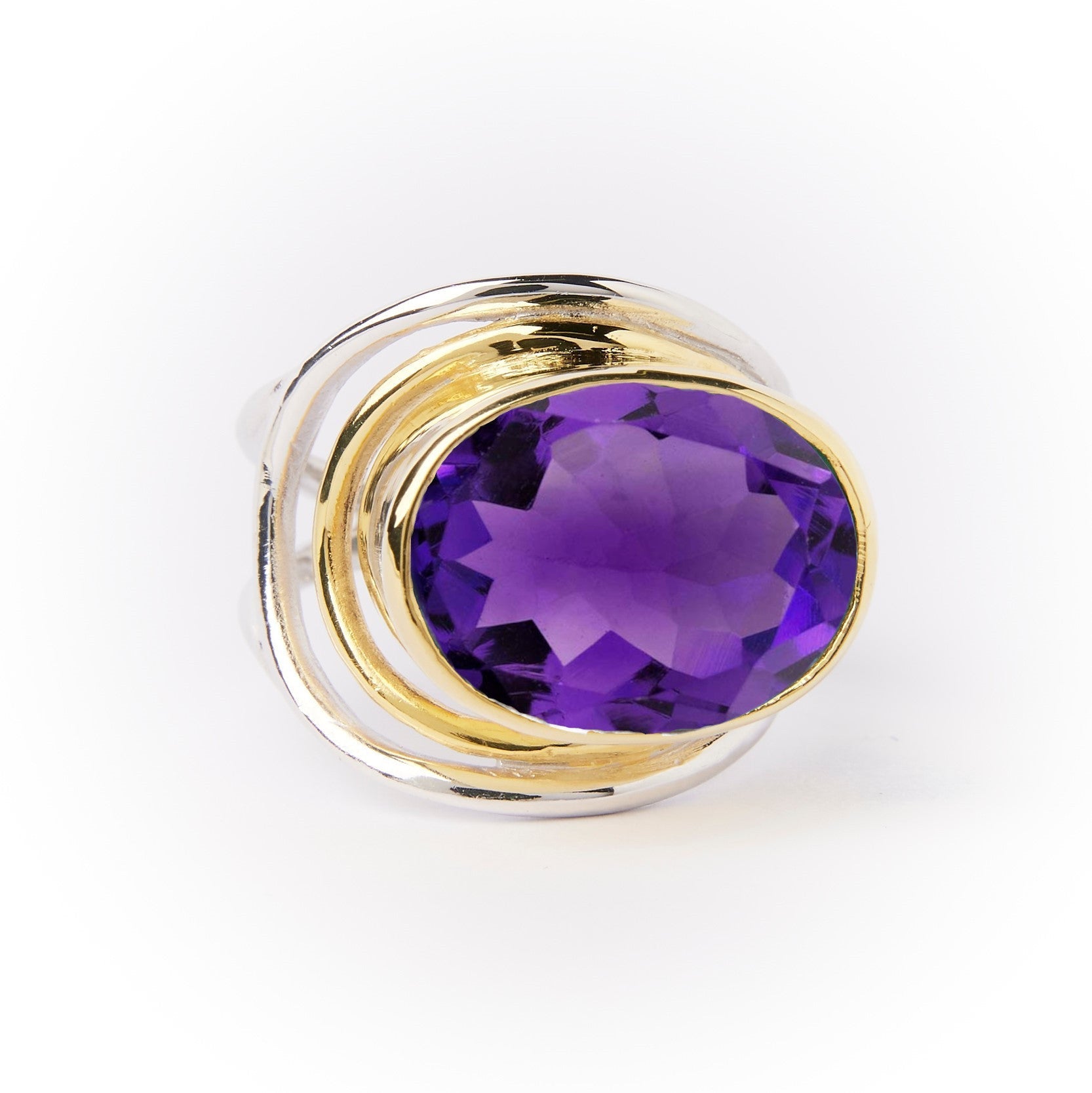 The Party Ring by Gallardo & Blaine Designs is a gold and silver chunky statement piece featuring a large faceted purple gemstone set in an intricate, swirling metal design, beautifully highlighted against the white background.
