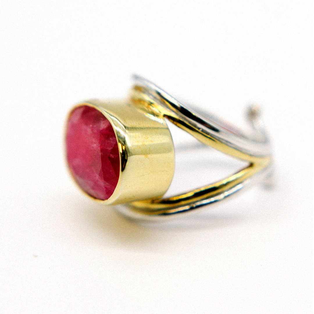 The Gallardo & Blaine Designs Party Ring, featuring a chunky gold and silver band with an intricate twisted design, showcases a large pink faceted gemstone in a cylindrical setting. This standout accessory adds depth and sparkle against its white backdrop
