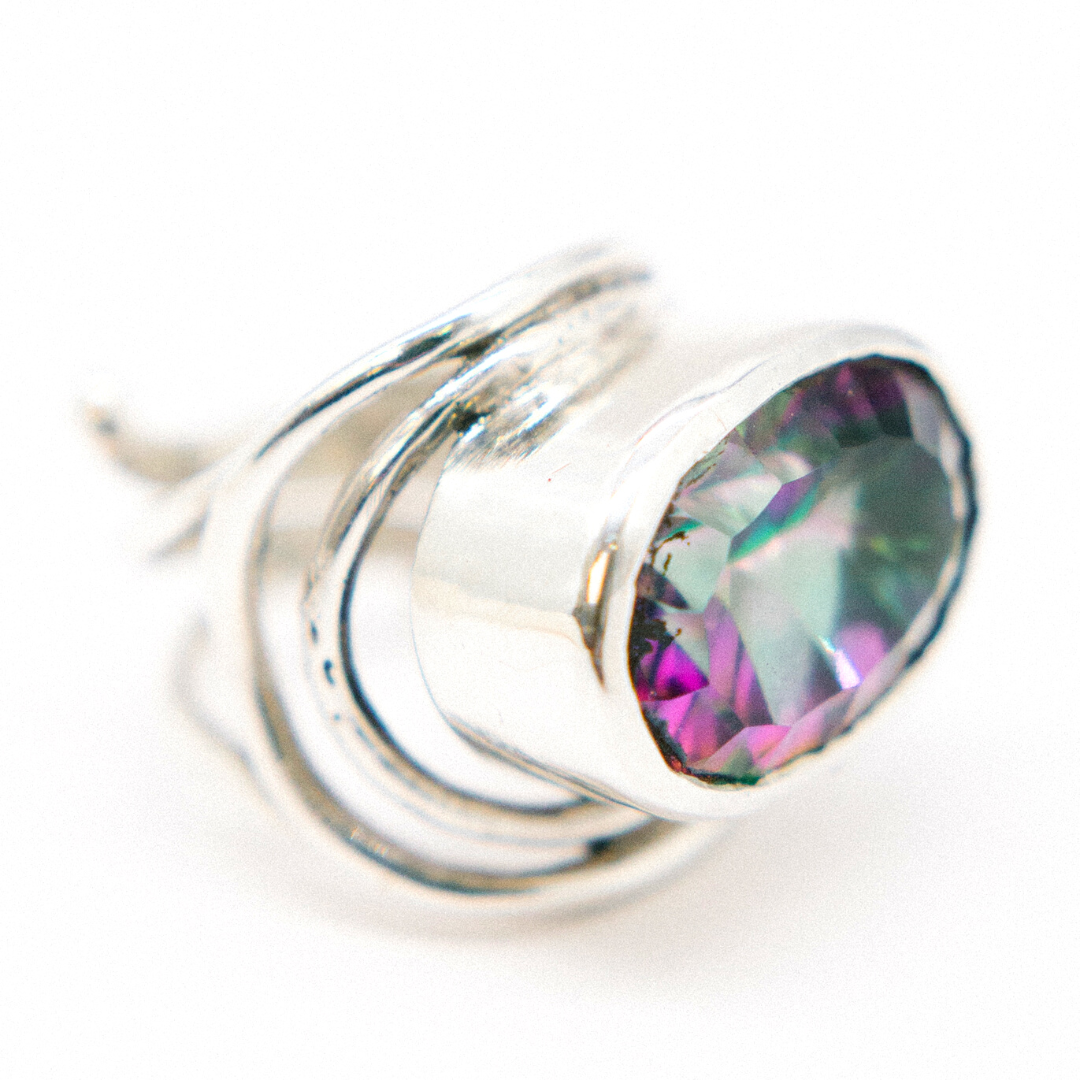 Close-up of a sterling silver & gold statement Gallardo & Blaine Designs Party Ring in various gemstones featuring a large, multi-colored gem. The stone exhibits shades of purple and green, with a faceted cut that catches the light. The band is elegantly 