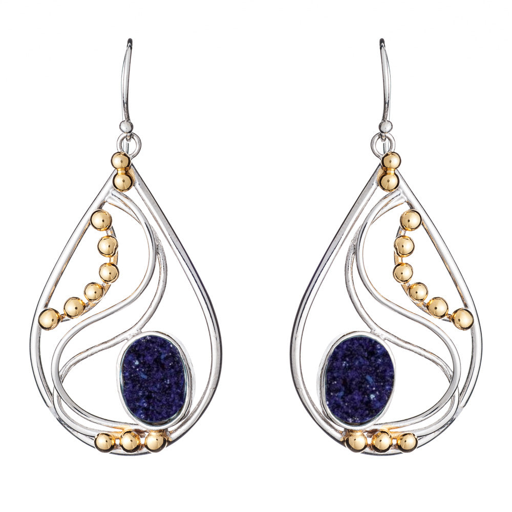 A pair of elegant drop earrings featuring silver-tone metal with curving lines and golden bead accents. The center of each Phoenix Earrings in various gemstones from Gallardo & Blaine Designs displays a deep blue oval gemstone, adding a striking contrast 