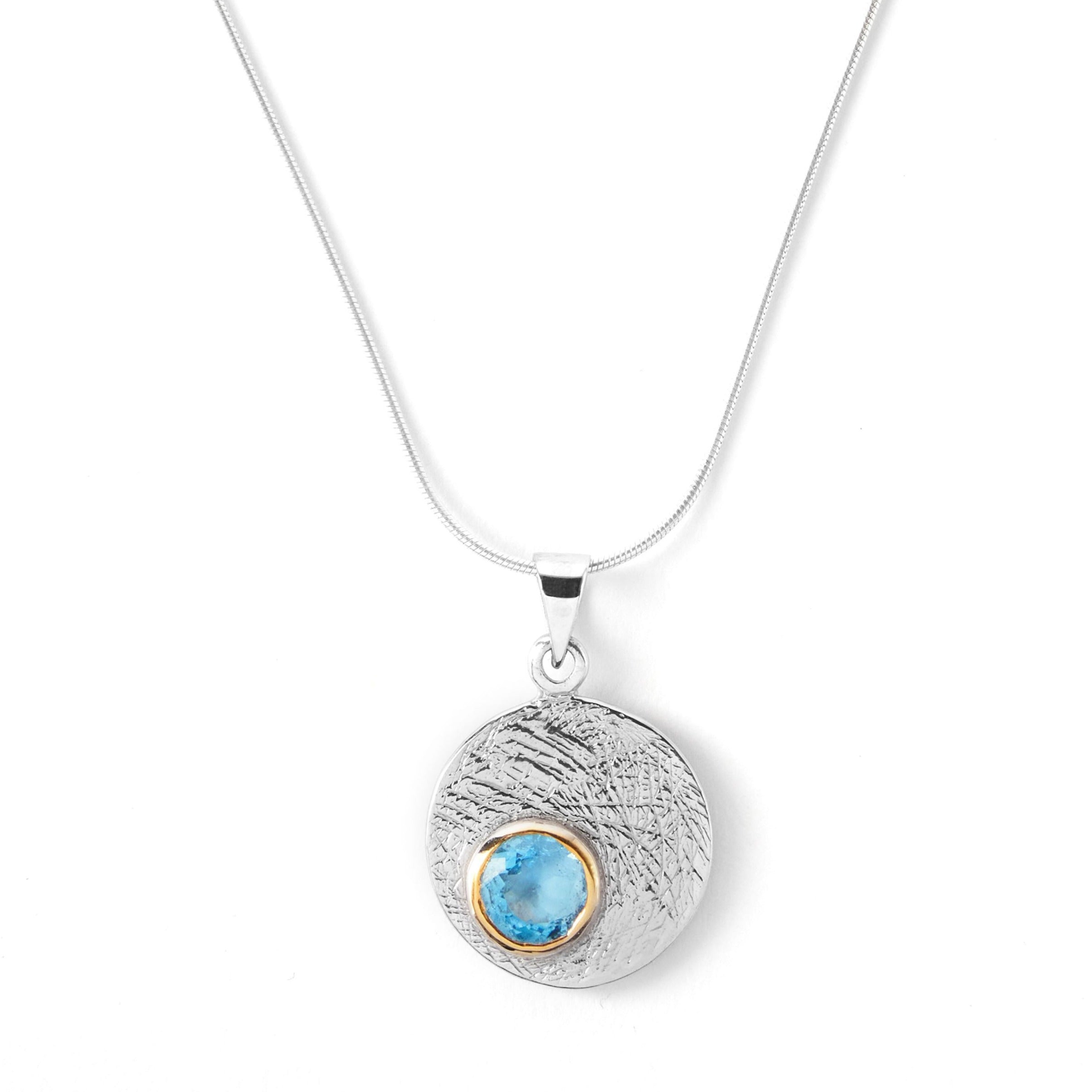 The Selene Necklace Silver - Small in various gemstones by Gallardo & Blaine Designs features a silver pendant with a textured surface and a small, embedded blue stone encircled by a gold bezel. Hanging gracefully from a Sterling silver chain, it combines