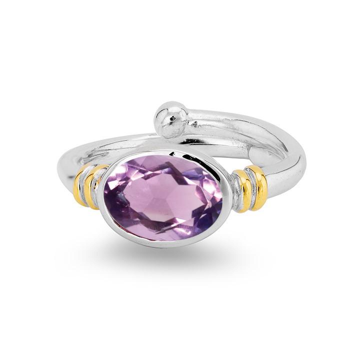 The Senna Ring in various gemstones by Gallardo & Blaine Designs is a silver adjustable ring featuring an oval cut purple gemstone in the center. The gemstone is held by a sleek, polished band with two small gold accents on each side. This elegant and mod