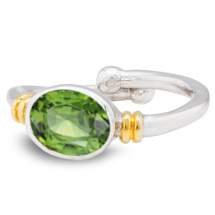 A Gallardo & Blaine Designs Senna Ring in various gemstones featuring an oval-shaped faceted green gemstone at its center. The gemstone is held by two gold accents on either side. The ring has a smooth, polished band that slightly overlaps at the back, ma