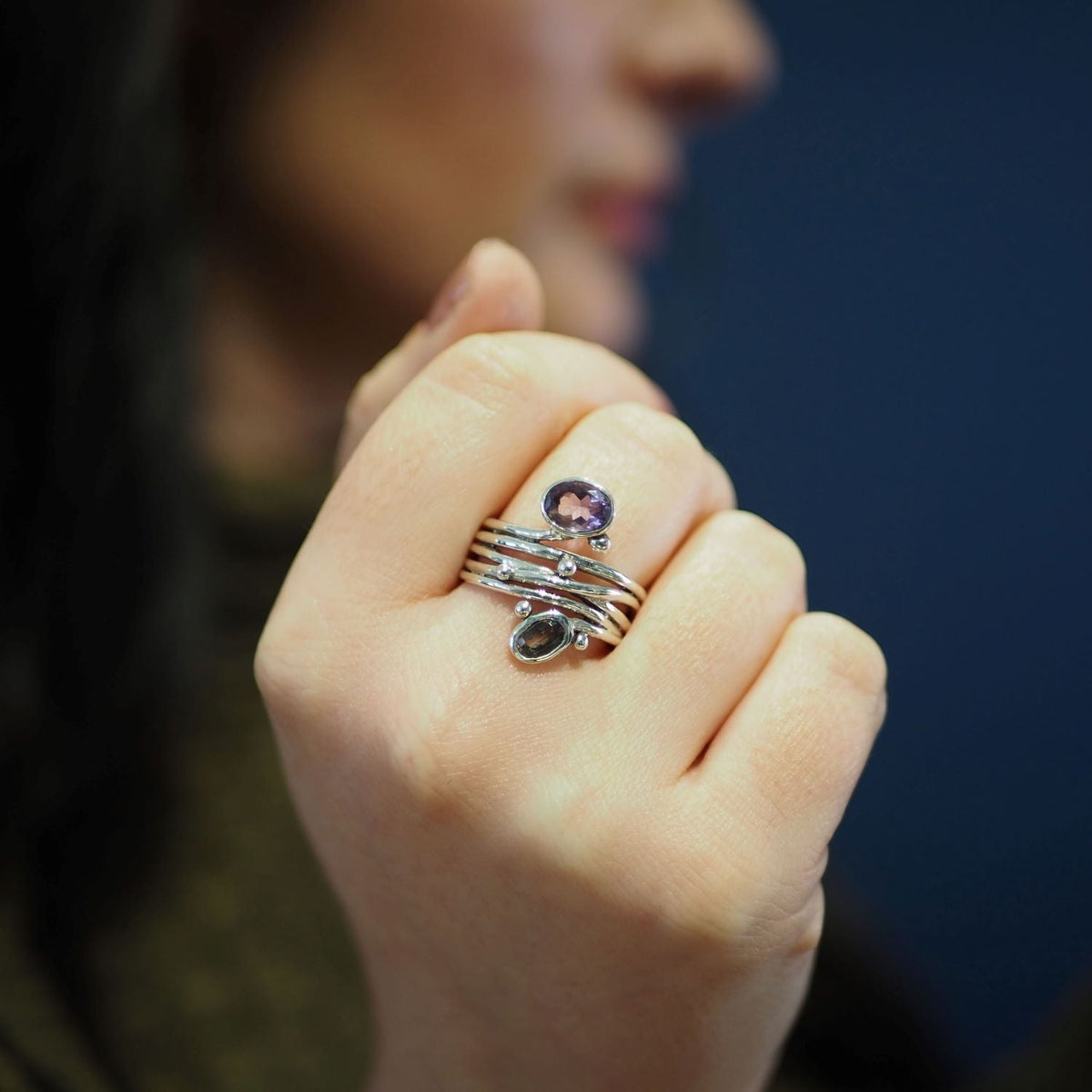 Close-up of a person's hand displaying silver rings with gemstones of varying colors and sizes on their fingers. Among them, a distinctive unique design featuring an adjustable Gallardo & Blaine Designs Snake Ring in Silver Gold & various gemstones stands
