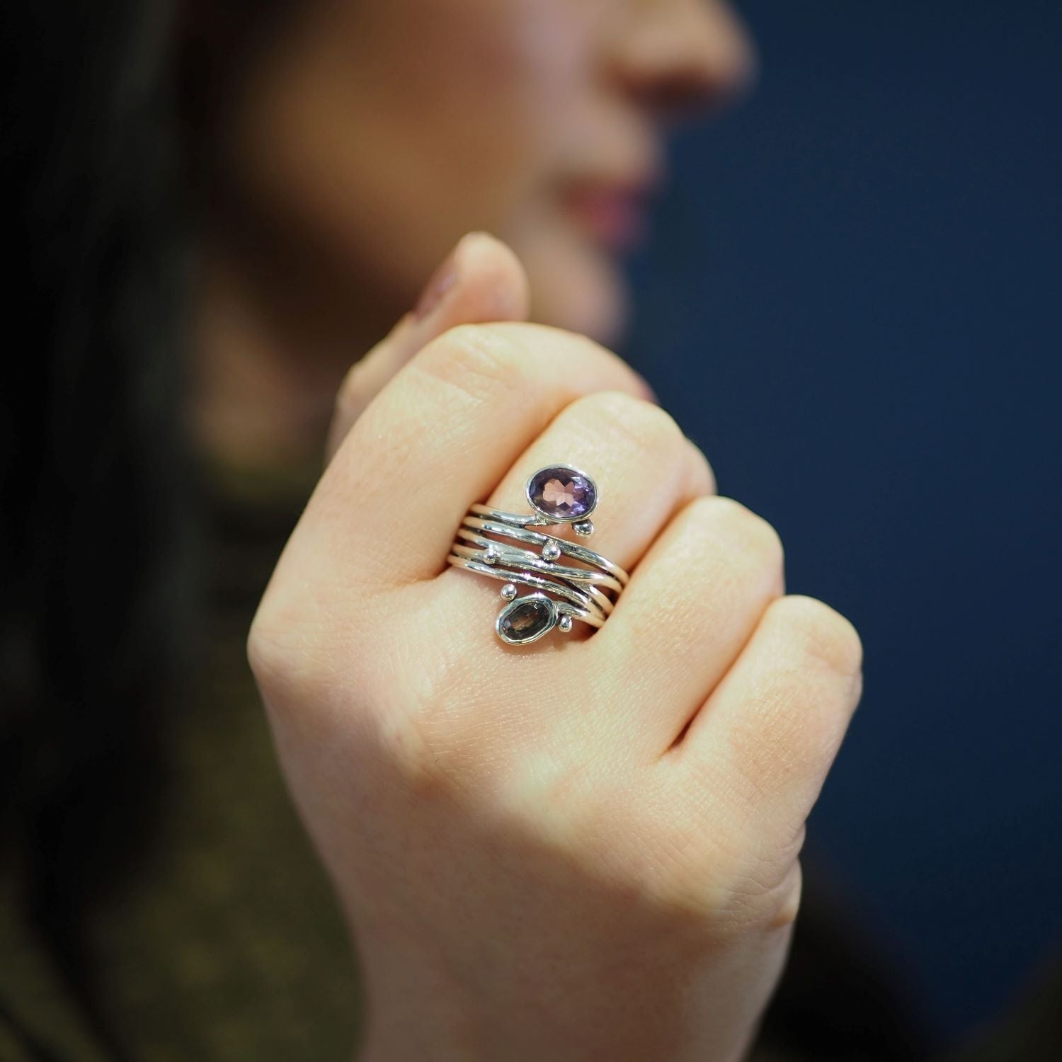 Close-up of a person's hand displaying silver rings with gemstones of varying colors and sizes on their fingers. Among them, a distinctive unique design featuring an adjustable Gallardo & Blaine Designs Snake Ring in Silver Gold & various gemstones stands