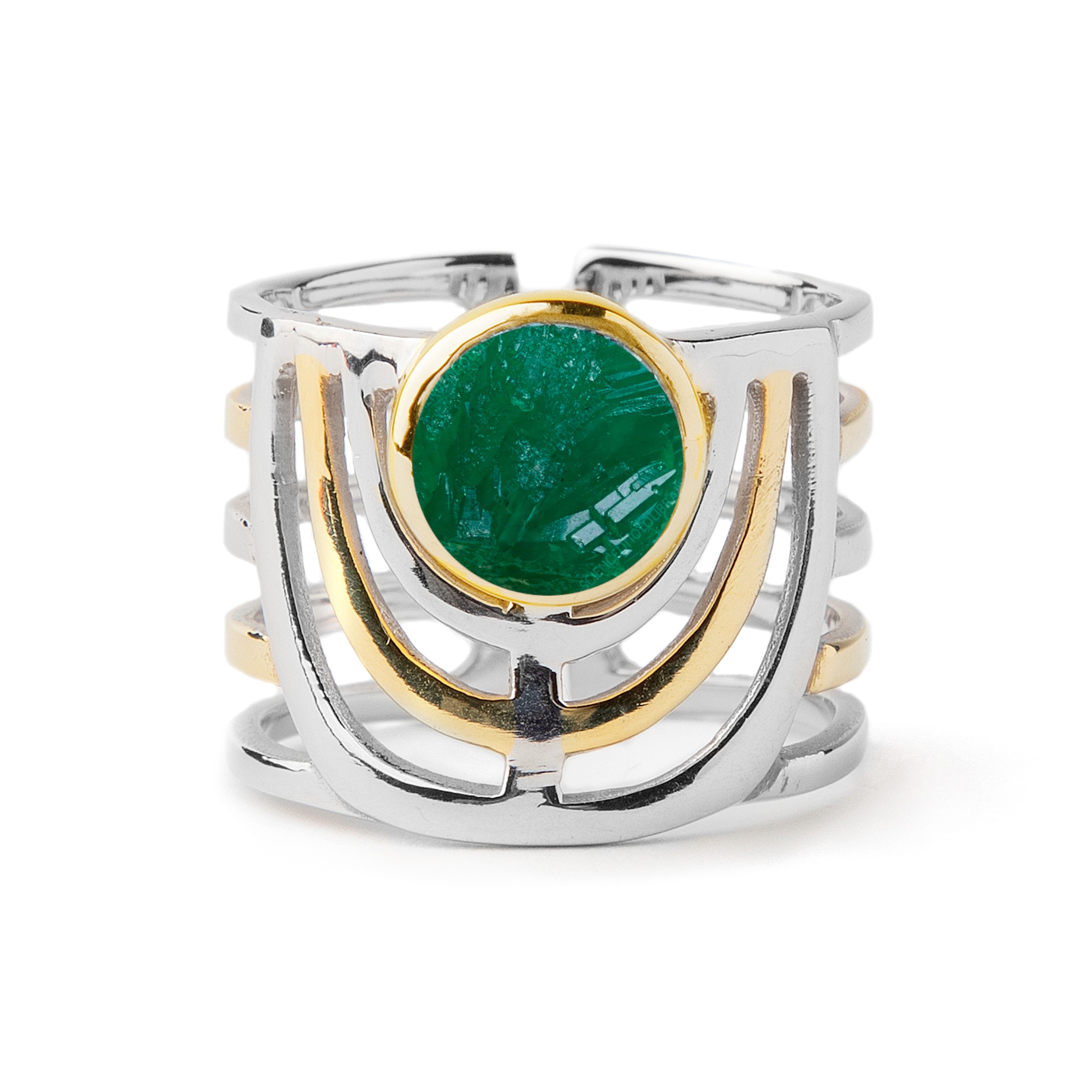 A bold jewellery design, the Solar Ring in various gemstones by Gallardo & Blaine Designs features an open band with a round, green gemstone in the center, surrounded by a gold bezel setting. The band splits into multiple parallel sections, creating an in