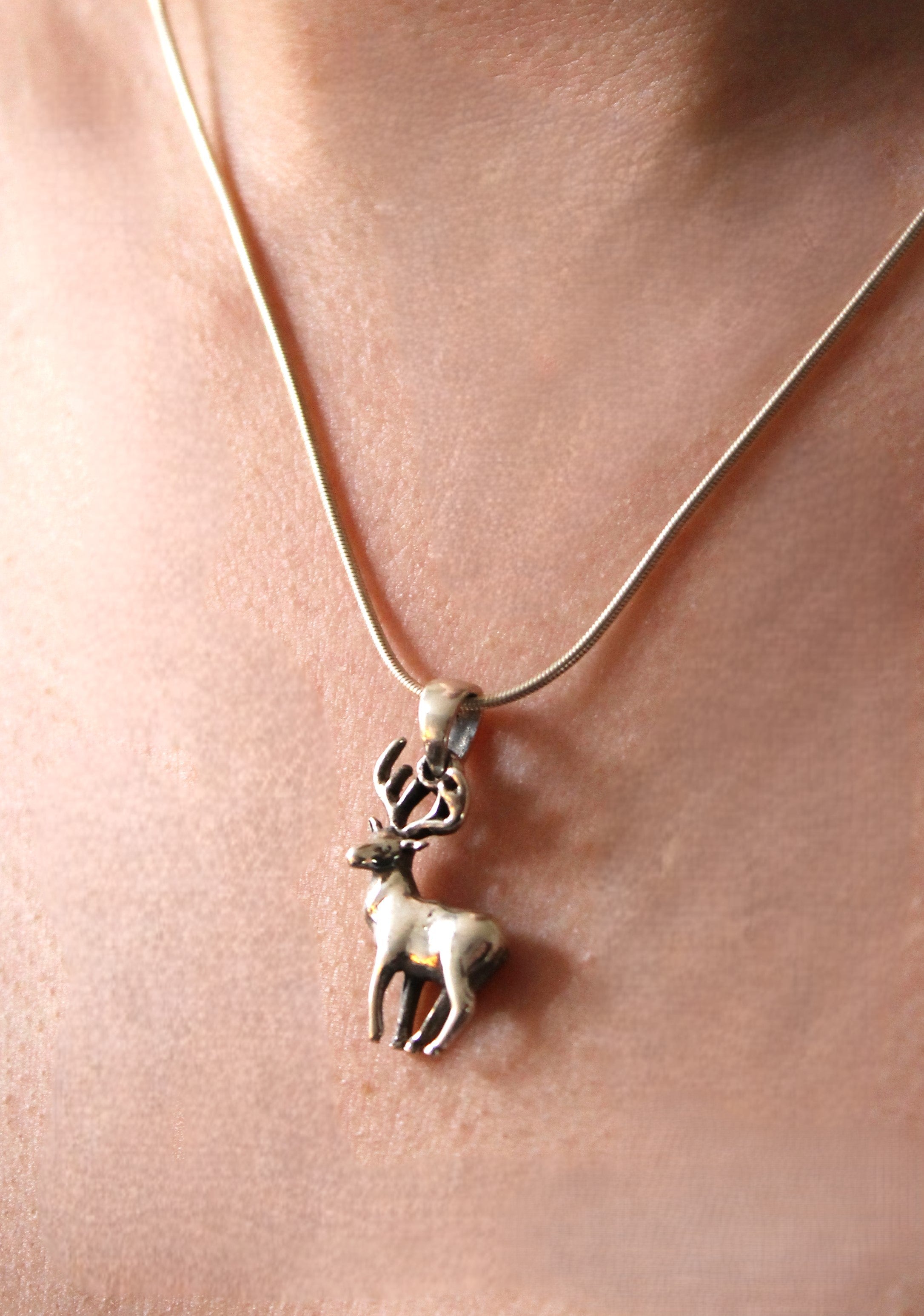 A close-up of the Wildlife Pendant - Stag With Chain by Watermelon Tropical, a silver necklace worn on bare skin—an ideal accessory for nature lovers.