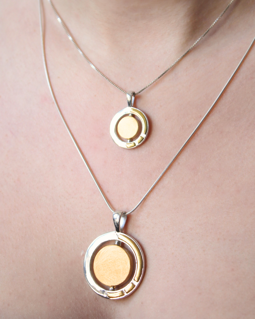 Two Gallardo & Blaine Designs Urú Small Pendant & Chain sterling silver necklaces with round gold and silver pendants—one higher, one lower—are worn together, inspired by Irish jewelry.
