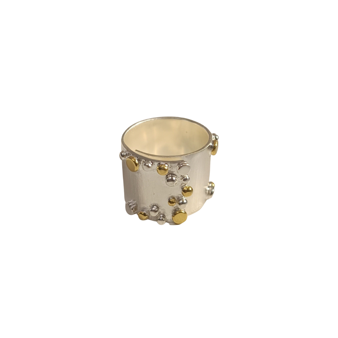 The Adjustable Iona Silver & Gold Ring by Gallardo & Blaine Designs features a wide silver band with a matte finish, scattered gold plate, and sterling silver orbs for a textured, modern look. The cylindrical band is smooth inside.