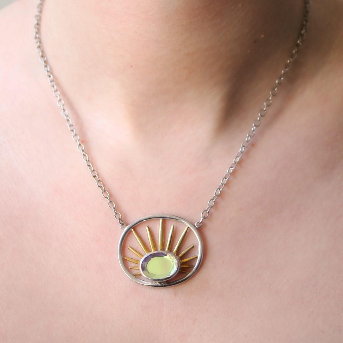 The Goddess Necklace Small by Gallardo & Blaine Designs features a circular pendant with a yellow-green gemstone and gold rays, elegantly crafted in sterling silver—an exquisite accessory for any neckline.